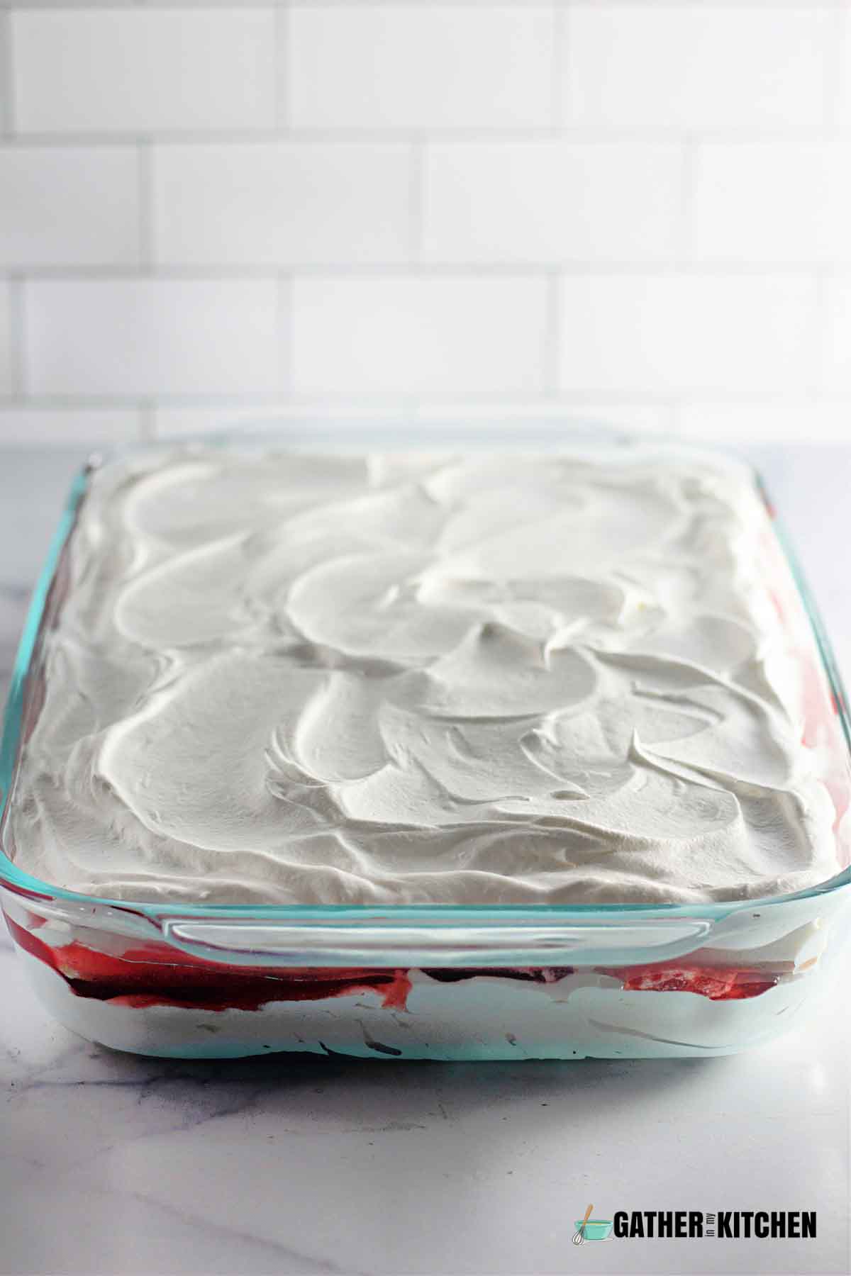A casserole dish of strawberry ice cream cake with cool whip on top.