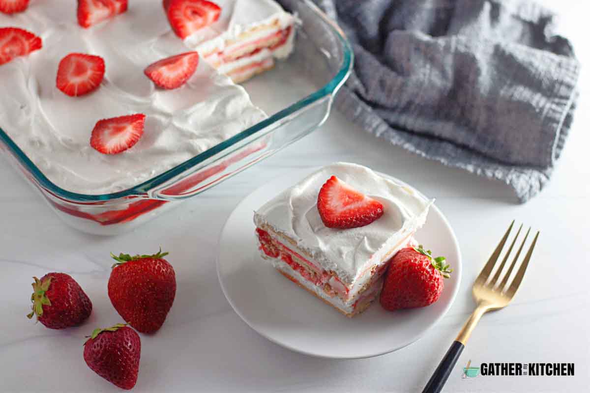 A slice of strawberry ice cream cake beside a whole tray