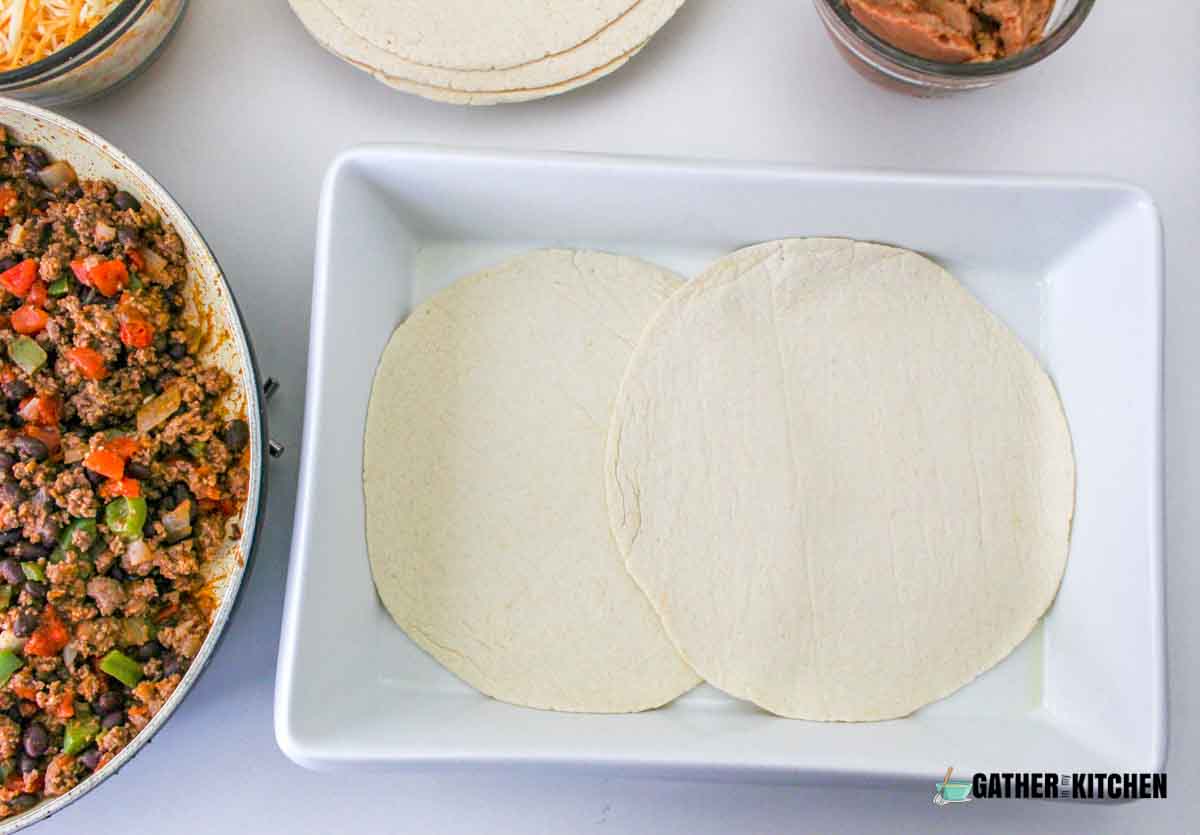 Two tortillas overlapping in the middle on bottom of casserole dish.