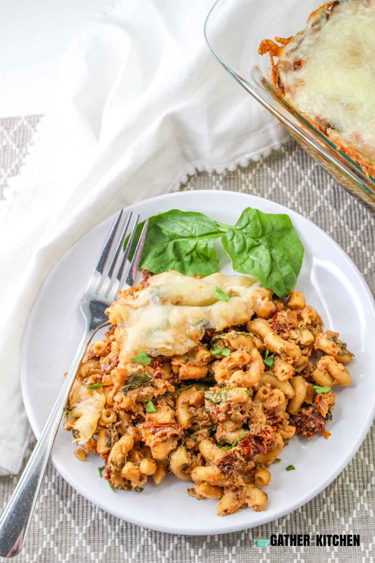 A serving of tuscan mac and cheese on a plate with basil and a fork on the side.
