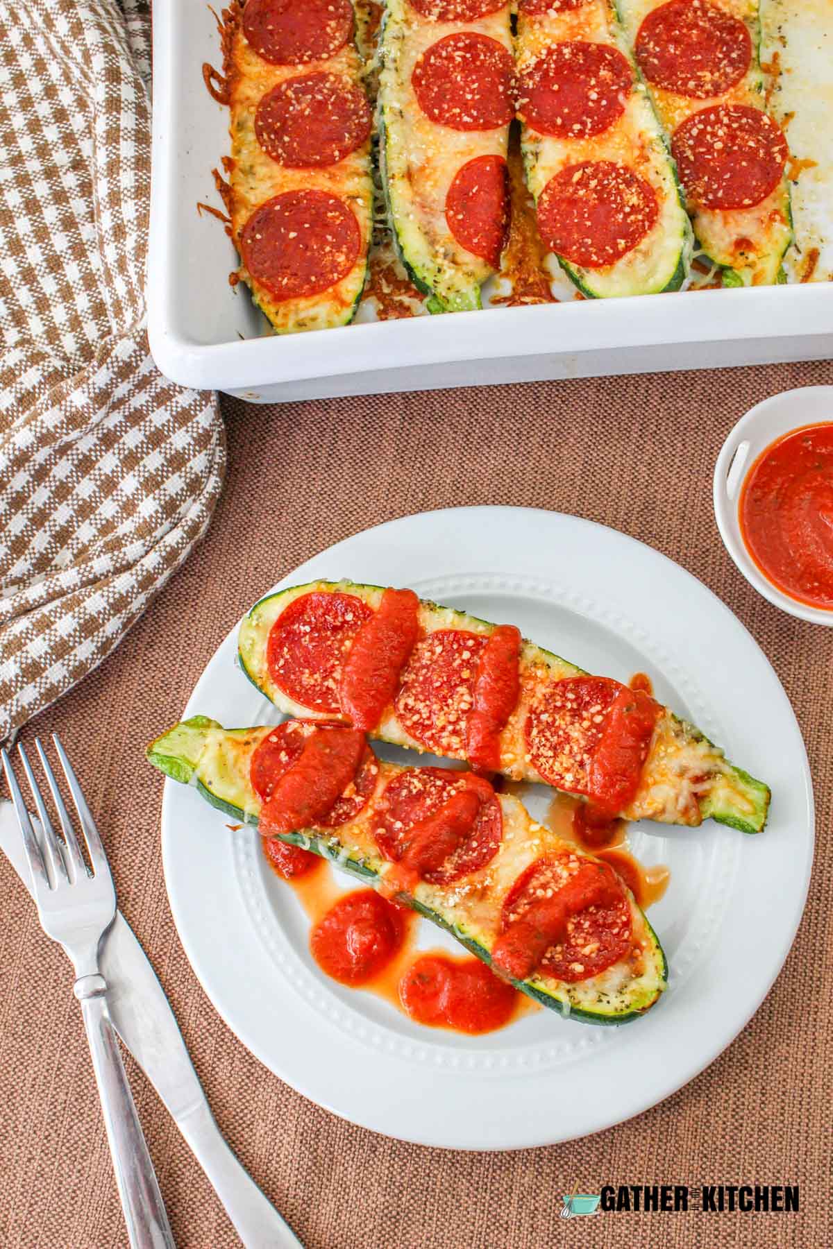Zucchini pizza boats on a plate with pizza sauce drizzled over the top.