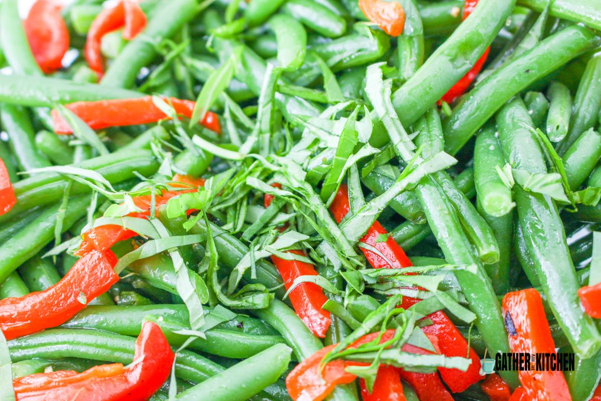 Green beans with sliced basil and red bell peppers on top.