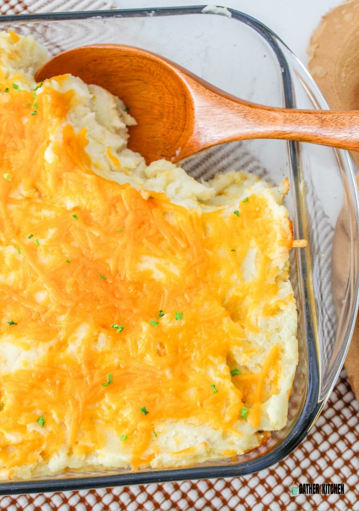 Mashed potato casserole in a baking dish with a serving taken out and a wooden spoon in it.