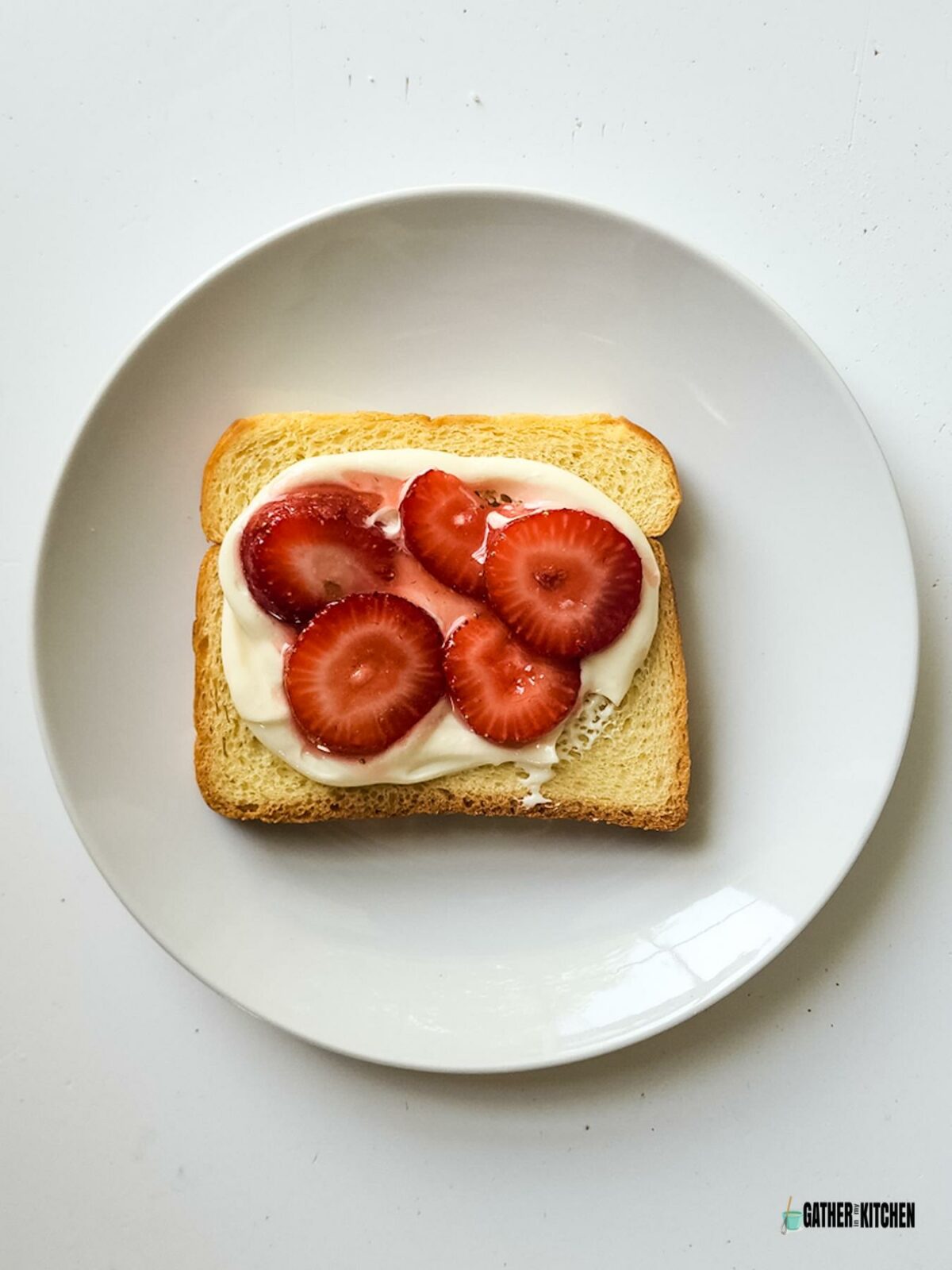 A piece of bread with cream cheese spread and strawberries.