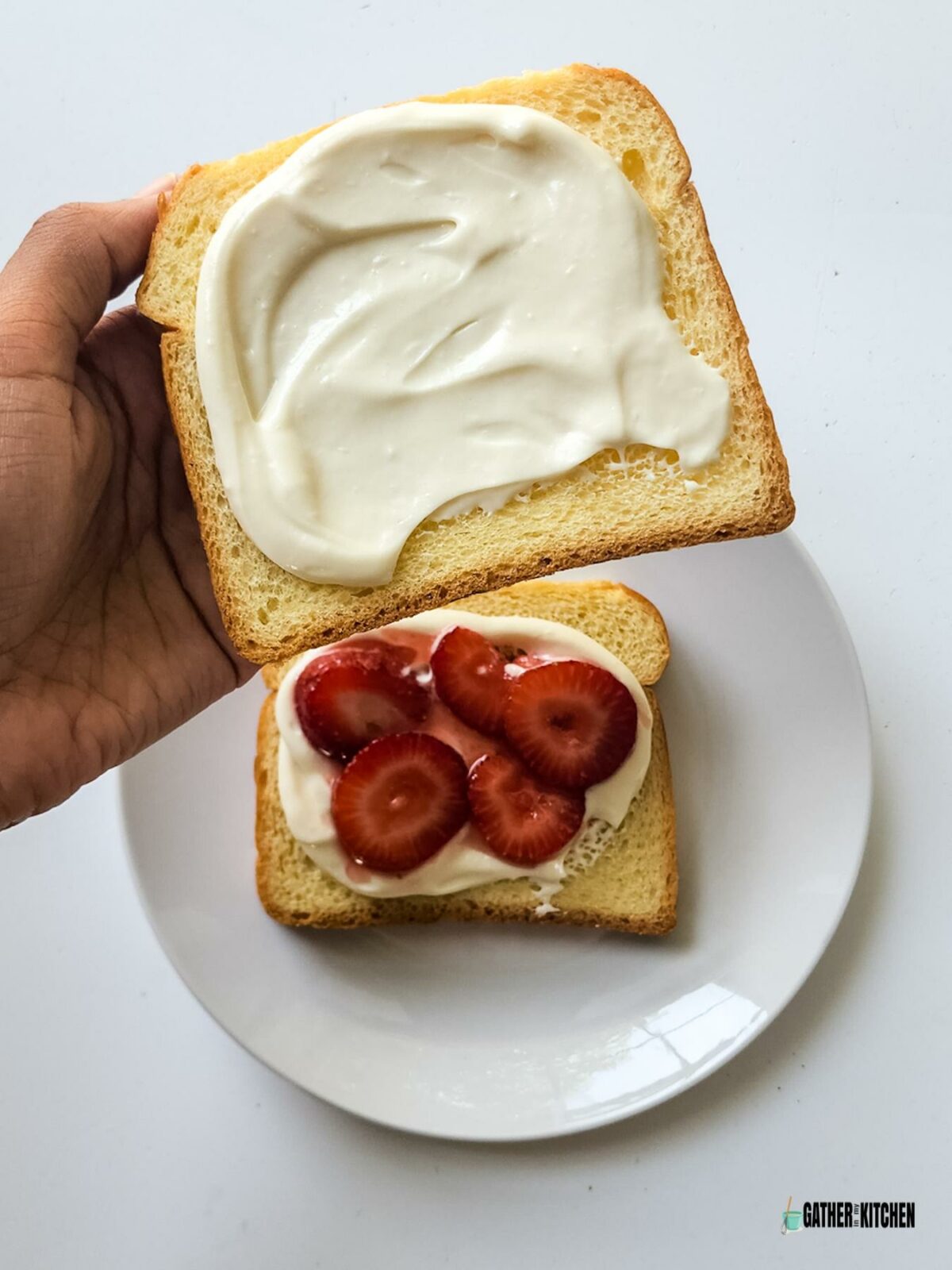 A piece of bread with cream cheese spread on it and a plate with a piece of bread with cream cheese and strawberries on it.