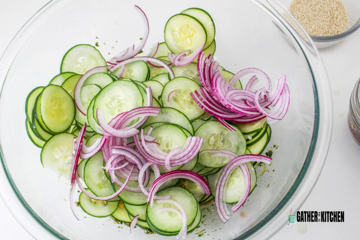 Top down view of sliced cucumbers and red onions in a bowl.