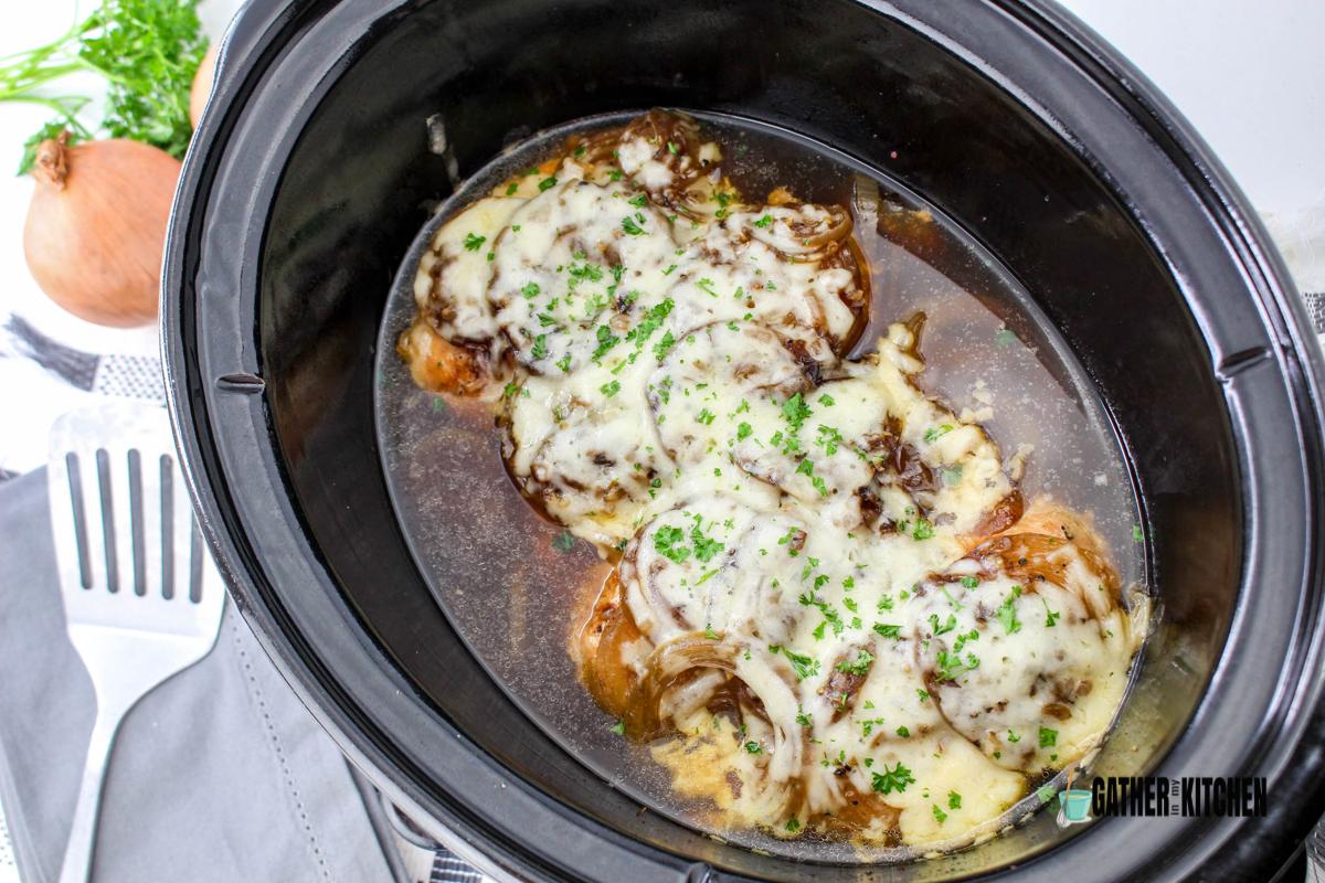 Cheese melted on top of cooked French onion chicken in slow cooker.