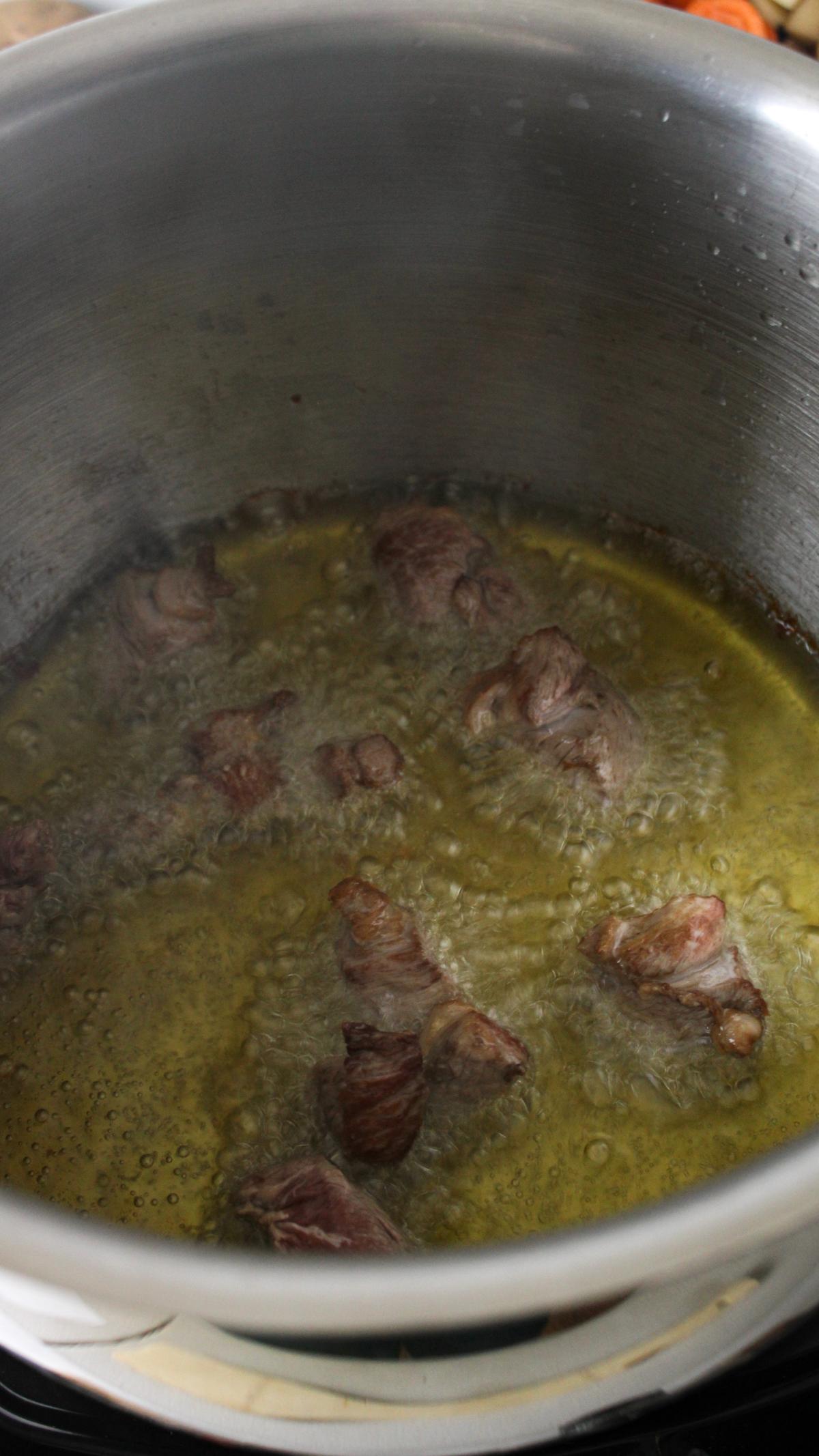Bottom of large stock pot with lamb cooking in oil.