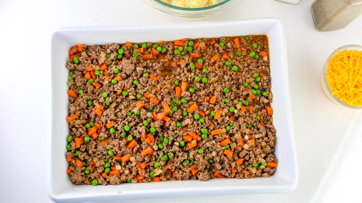 Casserole dish with meat mixture spread on bottom.