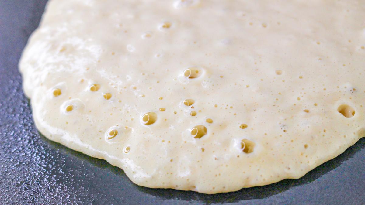 Pancake batter on a griddle with bubbles on top.