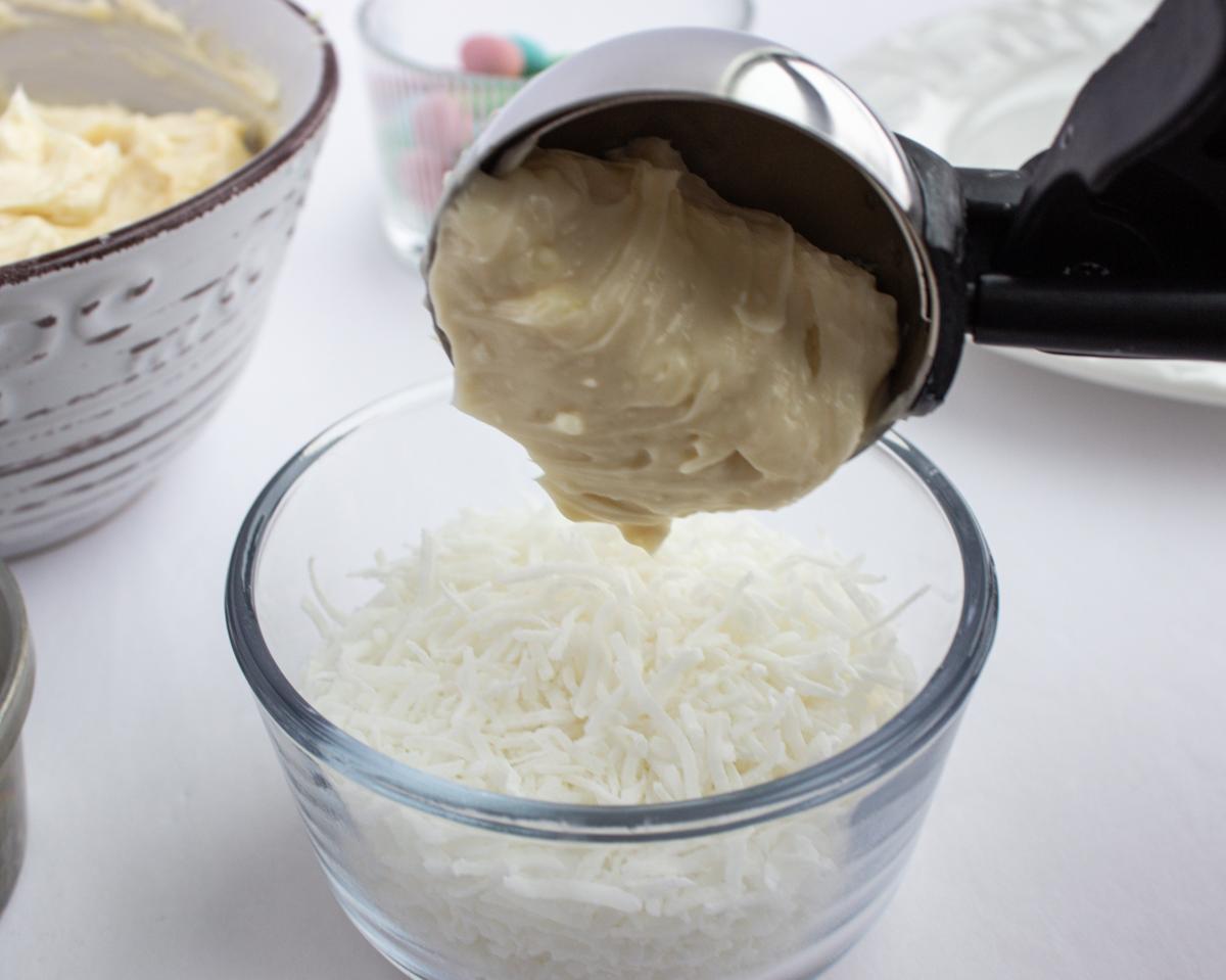Large scoop with cheese mix being plopped into shredded coconut.