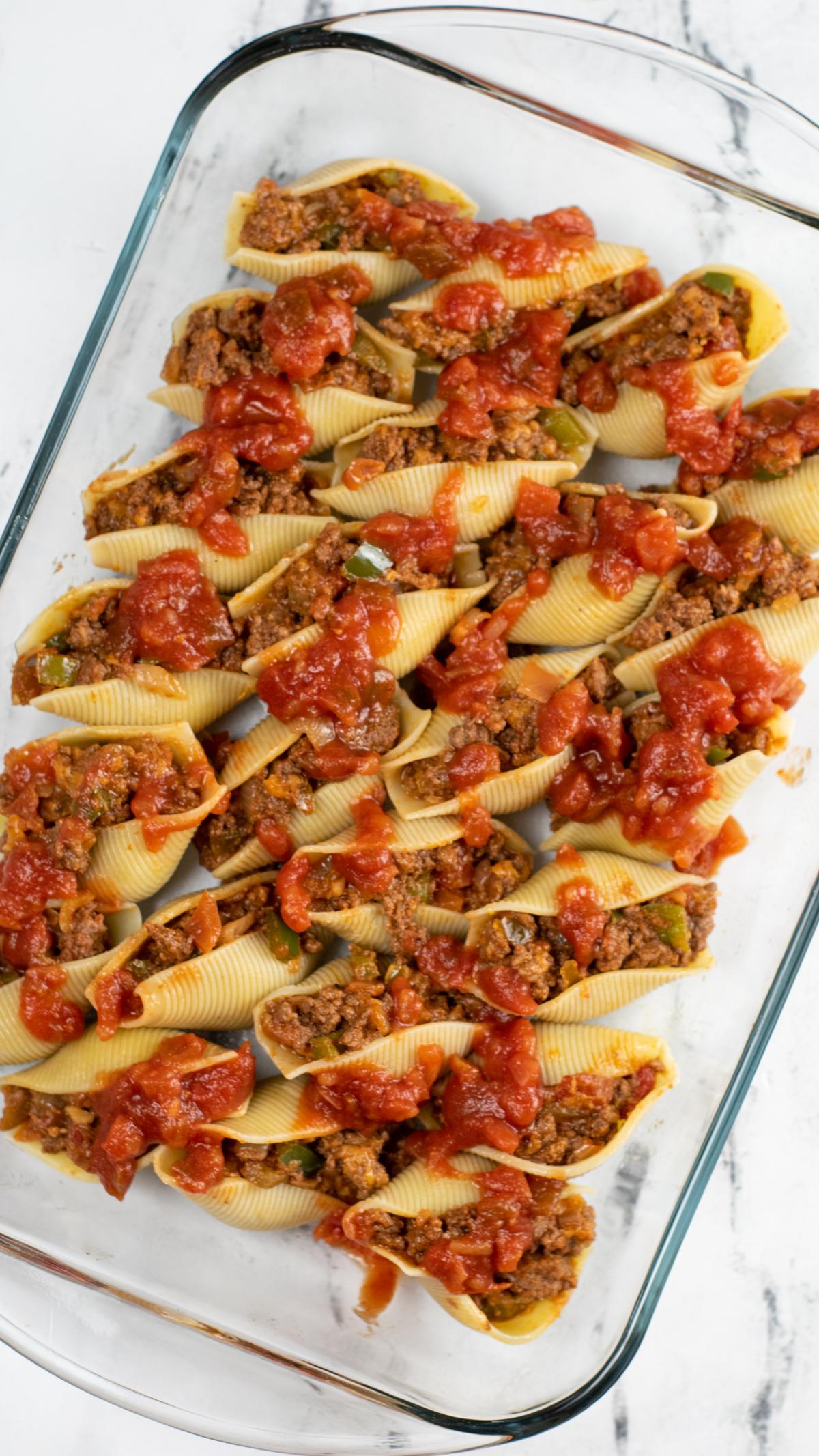 Filled shells with meat and drizzled with salsa in casserole dish.