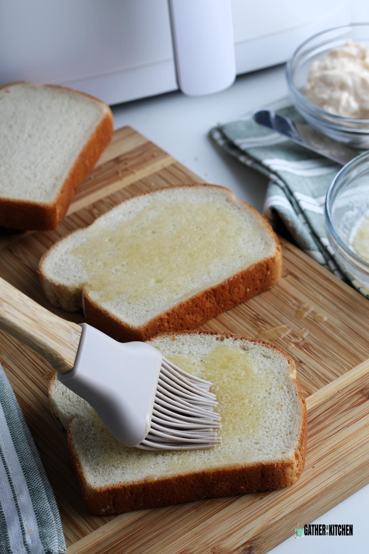 Pastry brush spreading melted butter on two halves of bread.