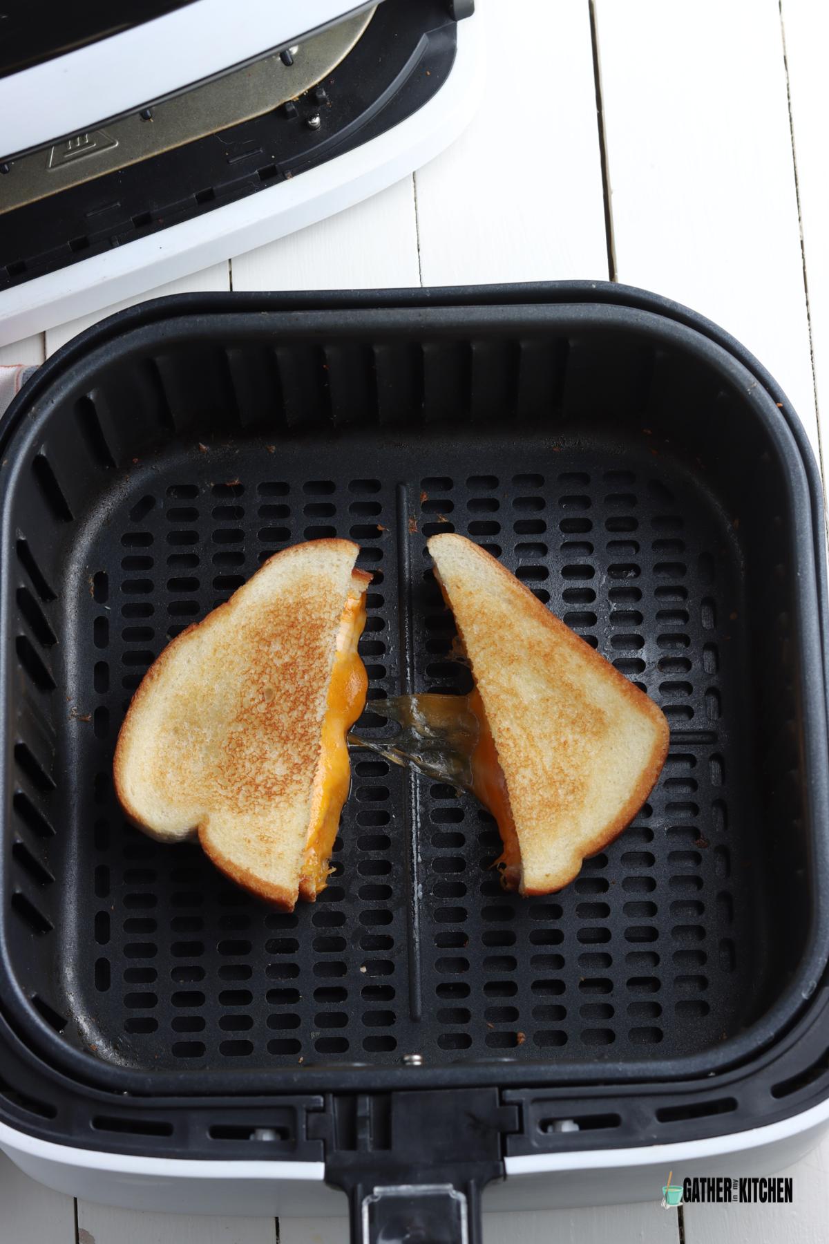 Grilled cheese sandwich cut in half in air fryer basket.