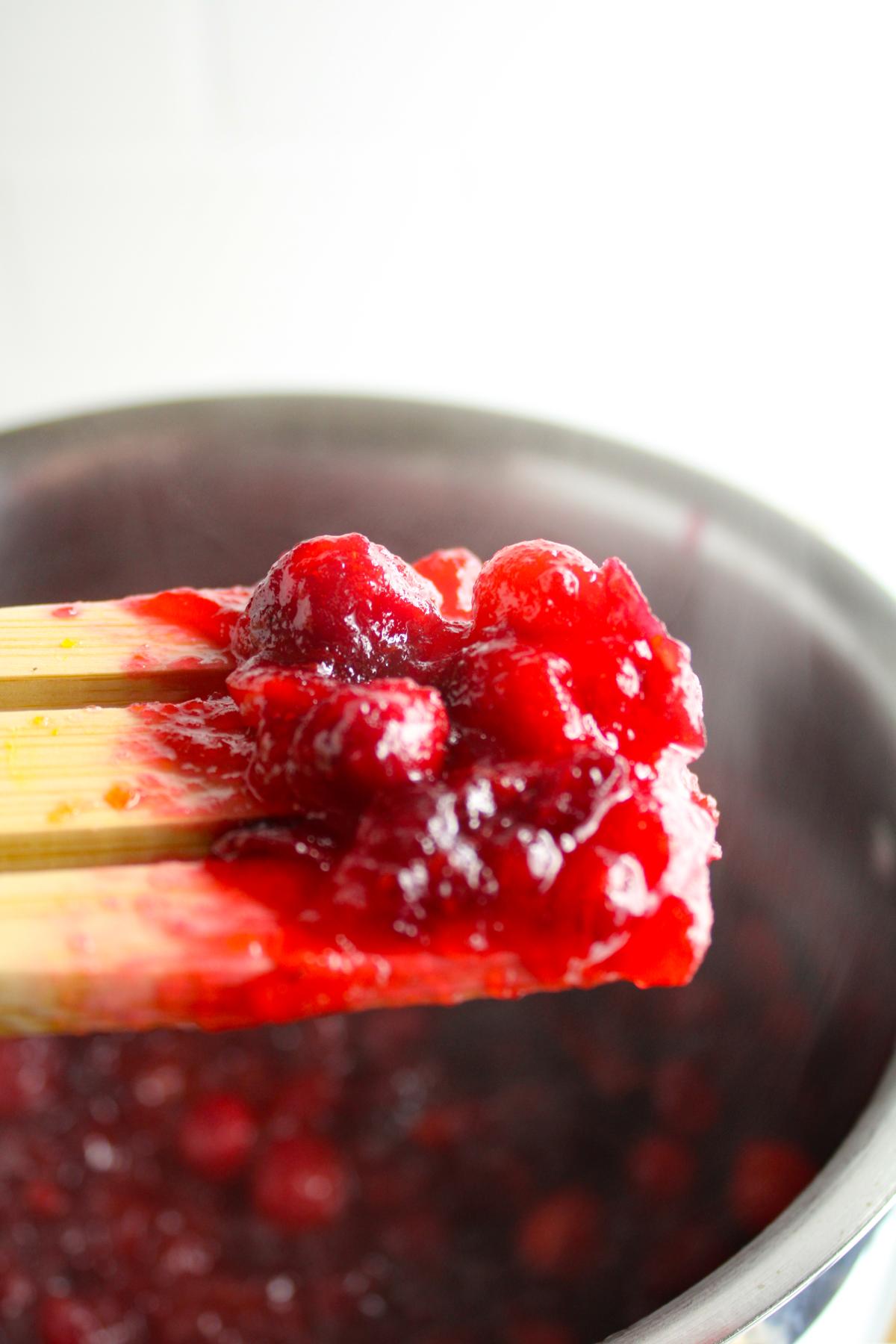 Wooden spoon holding up cranberry sauce from the pan.